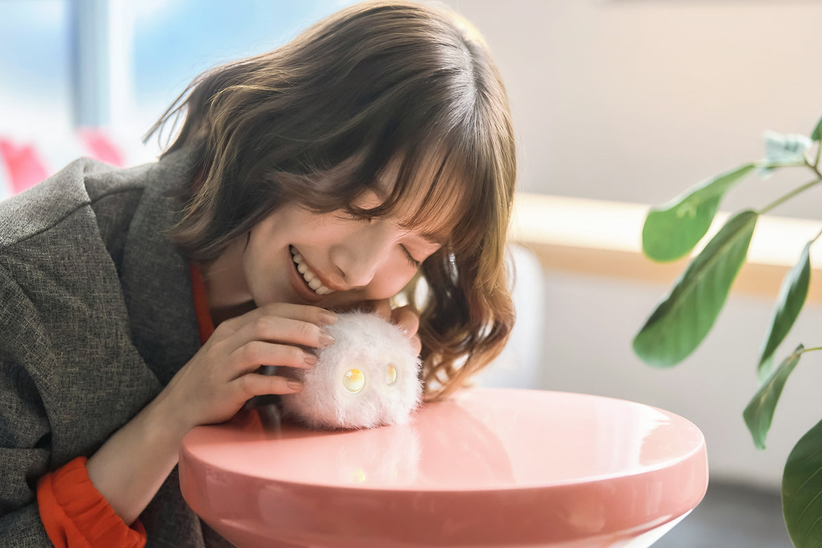 テーブルの白いフゾゾに顔を近づけて笑顔を見せる女性